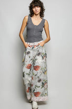 Load image into Gallery viewer, A model stands against a light gray studio background wearing a gray ribbed tank top and wide-leg floral pants with a white embroidered patch on the thigh.