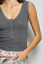 Load image into Gallery viewer, A close-up of a woman wearing a dark gray ribbed knit sleeveless henley top with a scalloped neckline, button placket, and chest pocket, paired with patterned jeans against a light gray background.