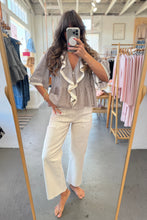 Load image into Gallery viewer, Woman taking a mirror selfie in a clothing store wearing a checkered blouse and white pants.