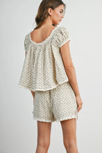 Load image into Gallery viewer, A woman modeling a matching two-piece set featuring a short-sleeve puff-sleeve top and shorts in a cream color with a small green floral pattern, shown from a three-quarters back view against a light gray studio background.