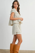 Load image into Gallery viewer, A woman modeling a matching two-piece outfit consisting of a short flutter-sleeve top and shorts in an off-white fabric with a small beige floral print, paired with tan knee-high boots against a plain white studio background.