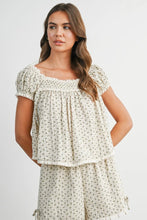 Load image into Gallery viewer, A woman modeling a cream-colored two-piece matching set with a small green floral print. The set includes a short-sleeve tiered top with puff sleeves and matching shorts, photographed against a plain light gray background.