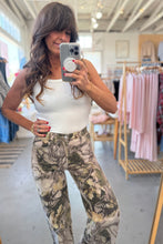 Load image into Gallery viewer, Woman taking a mirror selfie wearing a white top and camouflage pants in a store.