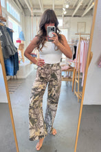 Load image into Gallery viewer, Woman taking a mirror selfie wearing a white top and patterned pants in a clothing store.