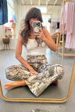 Load image into Gallery viewer, Woman taking a mirror selfie wearing a white top and patterned pants in a clothing store.
