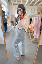 Load image into Gallery viewer, Person taking a mirror selfie wearing a white sweater with red trim and checkered pants in a clothing store.