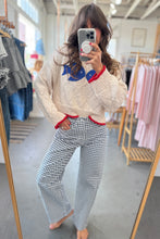Load image into Gallery viewer, Person wearing a cream sweater with colorful design and checkered pants in a clothing store.