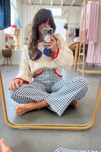 Load image into Gallery viewer, Woman sitting on the floor taking a mirror selfie wearing a colorful sweater and checkered pants.