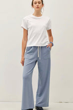 Load image into Gallery viewer, A woman modeling a white short-sleeve crewneck t-shirt and light blue wide-leg drawstring pants against a plain off-white studio background.