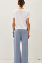 Load image into Gallery viewer, A woman shown from the back wearing a white short-sleeve cropped T-shirt and light blue wide-leg pants against a plain off-white studio background.