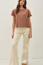 Load image into Gallery viewer, A woman modeling a short-sleeve crewneck t-shirt in a dusty rose color paired with cream-colored wide-leg jeans, standing against a plain off-white studio background.