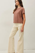 Load image into Gallery viewer, A woman modeling a short-sleeve crewneck t-shirt in a dusty rose color, paired with cream-colored wide-leg pants, against a plain off-white studio background.