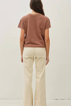 Load image into Gallery viewer, A woman shown from the back wearing a short-sleeve crewneck t-shirt in a muted terracotta brown and cream-colored wide-leg pants, standing against a plain off-white wall.