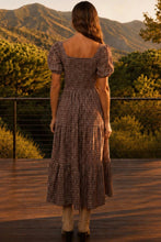 Load image into Gallery viewer, A woman stands on a wooden deck with a mountain and trees in the background, wearing a brown and beige gingham tiered midi dress with puff sleeves and a square neckline, viewed from behind.