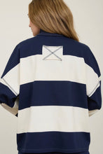 Load image into Gallery viewer, A woman shown from the back wearing a navy and off-white striped short-sleeve rugby-style shirt with a small stitched square patch on the upper back.