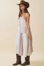 Load image into Gallery viewer, Woman wearing a long, light-colored dress with thin straps, brown boots, and a wide-brimmed hat on a beige background.