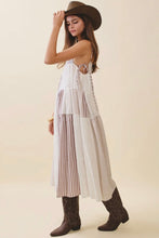 Load image into Gallery viewer, Woman wearing a long, light-colored dress with pleated layers, brown boots, and a wide-brimmed hat on a beige background.