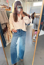 Load image into Gallery viewer, A woman takes a mirror selfie in a clothing boutique, wearing a light pink and white gingham long-sleeve blouse tucked into high-waisted, wide-leg blue jeans.