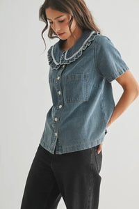 Woman wearing a denim shirt with ruffled collar on a plain background