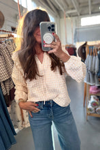 Load image into Gallery viewer, A woman taking a mirror selfie in a clothing boutique, wearing a cream and white gingham eyelet blouse with long puff sleeves and blue jeans.