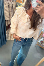 Load image into Gallery viewer, A woman takes a mirror selfie in a clothing store, wearing a cream and white gingham eyelet blouse with a ruffled collar and blue jeans.