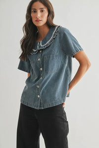 Woman wearing a denim shirt with lace trim on a plain background