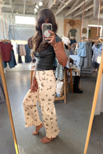 Load image into Gallery viewer, A woman takes a mirror selfie in a clothing boutique, wearing cream wide-leg pants with a black bird print and a dark gray t-shirt.