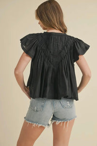 Woman wearing a black blouse with ruffled sleeves and denim shorts on a beige background