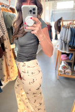 Load image into Gallery viewer, A woman takes a mirror selfie in a clothing store, wearing a fitted dark gray short-sleeve top and cream-colored pants with a small bird print.