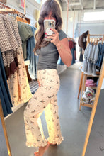 Load image into Gallery viewer, A woman takes a mirror selfie in a clothing boutique wearing cream ruffled wide-leg pants with a black bird print and a dark gray t-shirt. Clothing racks are visible in the background.