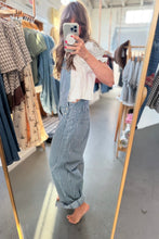 Load image into Gallery viewer, A woman takes a mirror selfie in a clothing boutique, wearing a white short-sleeve crop top and blue-and-white vertically striped wide-leg overalls. Clothing racks are visible on both sides of the store aisle.