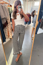 Load image into Gallery viewer, A woman takes a mirror selfie in a clothing boutique, wearing a white short-sleeve knit top and black-and-white gingham wide-leg pants.