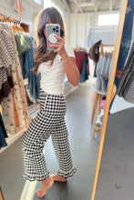 Load image into Gallery viewer, A woman takes a mirror selfie in a clothing boutique, wearing black and white gingham wide-leg pants with a ruffled hem, a white ribbed short-sleeve top, and barefoot.