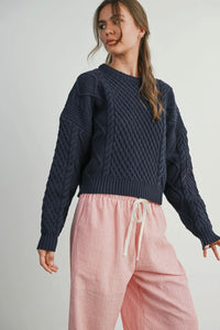 Woman wearing a navy blue knitted sweater and pink pants on a plain background