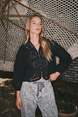 Woman wearing a black cardigan and patterned pants standing under a textured roof.