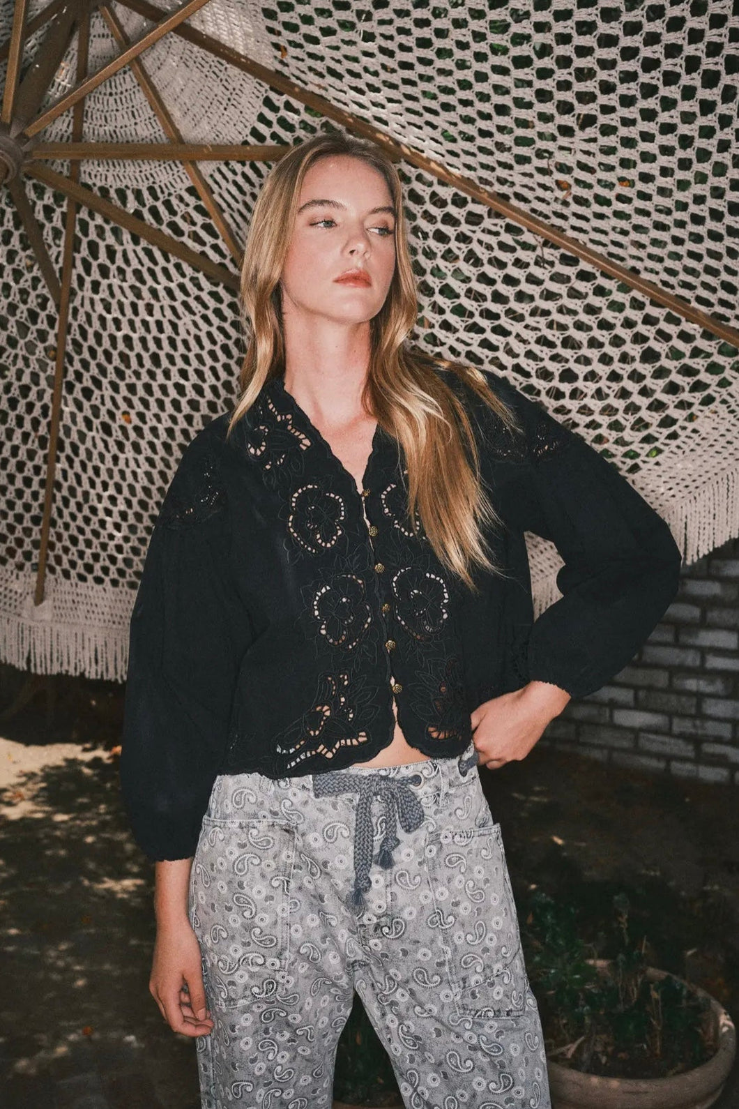Woman wearing a black cardigan and patterned pants standing under a textured roof.