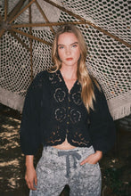 Load image into Gallery viewer, Woman wearing a black embroidered jacket and patterned pants standing under a textured canopy.