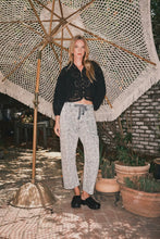 Load image into Gallery viewer, Woman standing under a large decorative umbrella in an outdoor setting with plants and a textured wall.