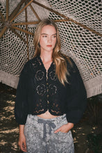 Load image into Gallery viewer, Woman wearing a black embroidered jacket and patterned pants standing under a textured canopy.