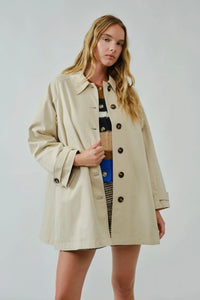 Woman wearing a beige trench coat against a plain background