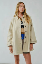 Load image into Gallery viewer, Woman wearing a beige trench coat over a patterned dress on a plain background