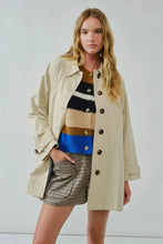 Load image into Gallery viewer, Woman wearing a beige trench coat over a colorful sweater and plaid skirt on a white background