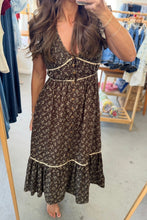 Load image into Gallery viewer, A woman takes a mirror selfie in a boutique wearing a dark brown floral midi dress with cream ruffle trim and a button-up front.