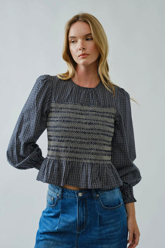 Woman wearing a black and white checkered blouse with a peplum waist and blue jeans on a plain background