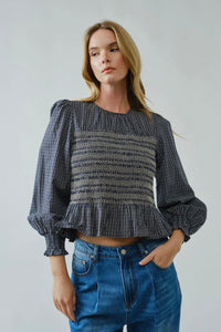 Woman wearing a black and white checkered blouse with puffed sleeves and blue jeans on a plain background