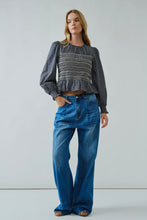 Load image into Gallery viewer, Woman wearing a patterned top and blue jeans against a plain background