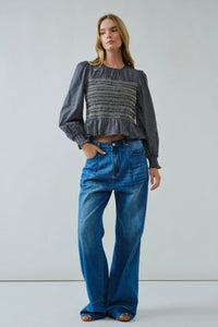 Woman wearing a patterned top and blue jeans against a plain background