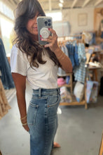 Load image into Gallery viewer, A woman taking a mirror selfie in a clothing boutique, wearing a white short-sleeve crewneck t-shirt and a high-waisted blue denim skirt.