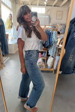 Load image into Gallery viewer, A woman takes a mirror selfie in a boutique clothing store, wearing a white short-sleeve t-shirt and high-waisted, wide-leg blue jeans with rolled cuffs.