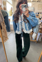 Load image into Gallery viewer, A woman takes a mirror selfie in a clothing boutique, wearing a light blue cropped denim jacket with white lace embroidery and tie-front detailing, paired with dark green wide-leg pants.